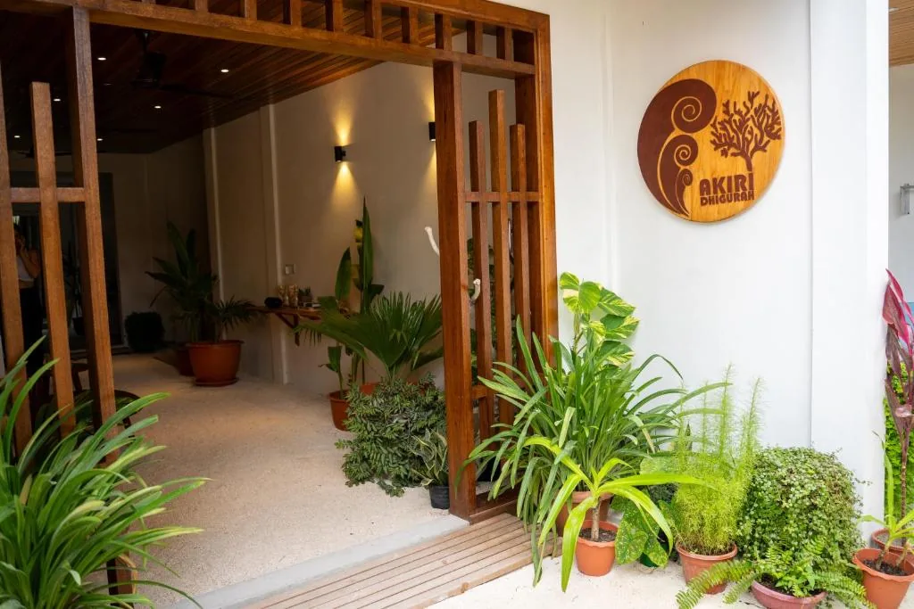 Open wooden door to akiri dihurani with potted tropical plants indoor seating and a coral tree logo on the wall at akiri dhigurah in dhigurah maldives