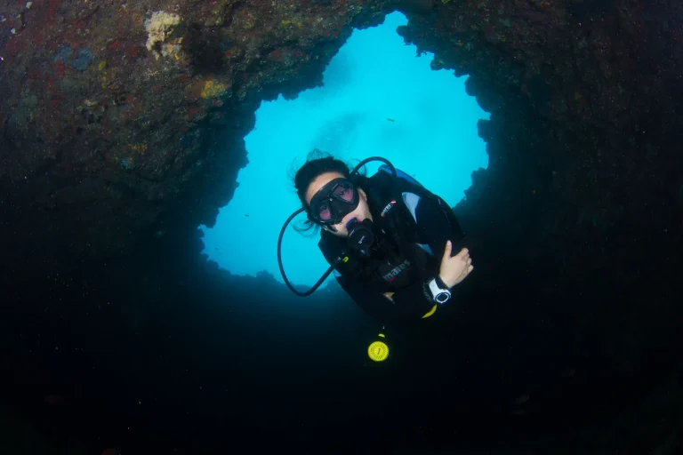 Scuba diver framed by a blue opening in a dark reef cave in the Blue Hole near Amilla Maldives