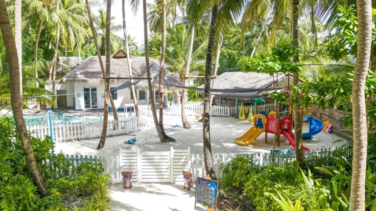 Aerial view of a kids club with a pool, playground and white buildings among palms at Amilla Maldives
