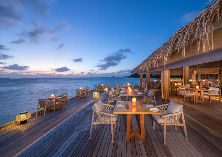 Open deck with candlelit tables over the water at dusk at SPICE restaurant, Anantara Kihavah
