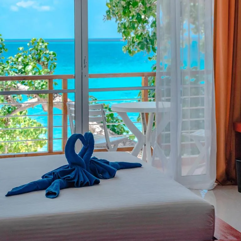 Ocean-view room with balcony table, sheer curtains and towel swans on the bed at Athiri Beach, Dhigurah, Maldives