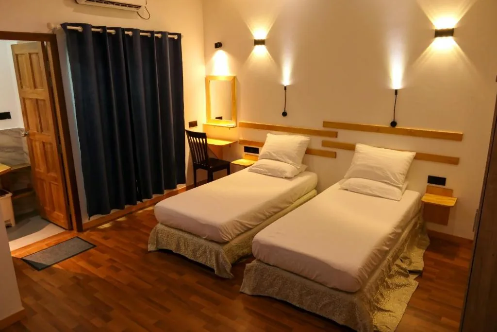 Twin room with two single beds, navy curtains, wall sconces, wooden headboard, bedside shelves and hardwood floor at Ayira Maldives, Feridhoo, Maldives