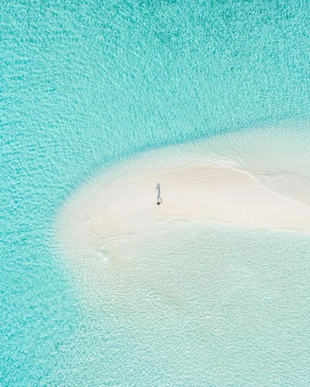 Aerial view of a small sandy islet with turquoise lagoon, a person standing on the sand and a small wooden raft on the water at Beach Stone, Gulhi, Maldives