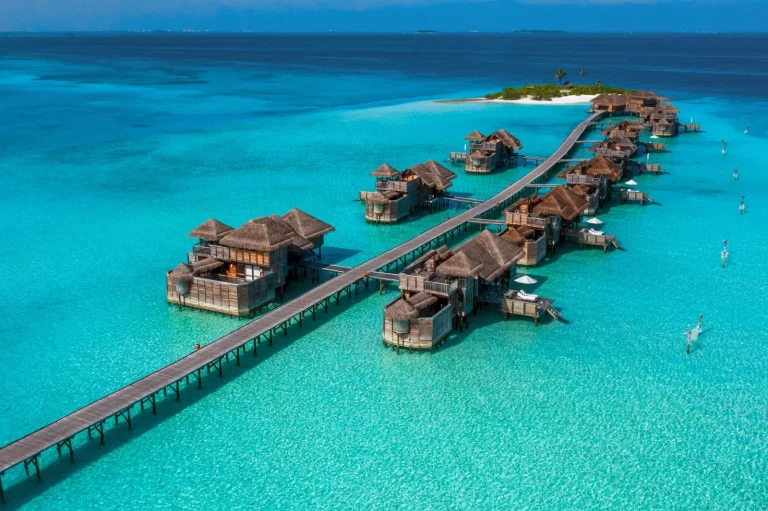 Aerial view of Gili Lankanfushi's all-overwater villas joined by a long wooden jetty over a pale lagoon, North Malé Atoll, Maldives
