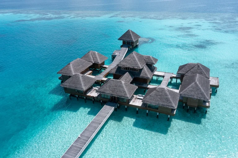 Aerial view of overwater villas with private pools at Huvafen Fushi, joined by a wooden jetty over a bright turquoise lagoon, North Malé Atoll