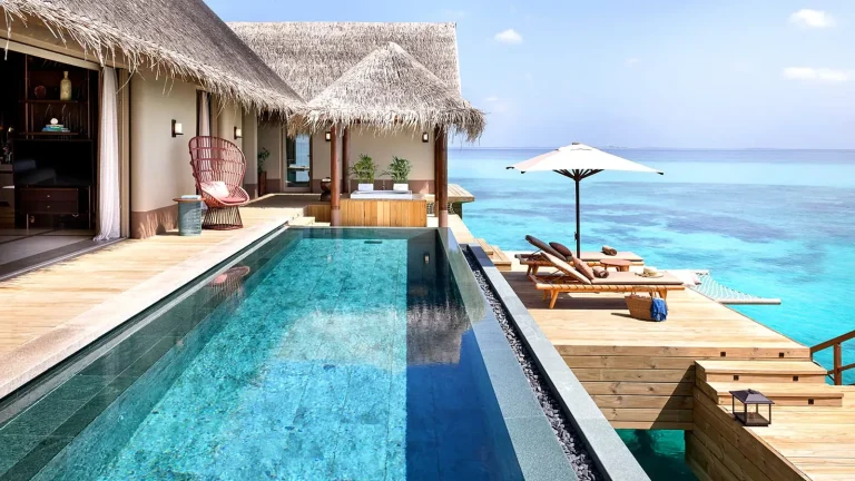 Infinity pool and teak deck of a three-bedroom ocean villa at JOALI Maldives with thatched roof and the Raa Atoll lagoon beyond
