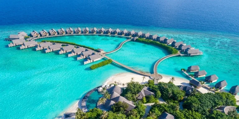 Aerial view of Milaidhoo Maldives water pool villas curving around a lagoon beside a small green island in Baa Atoll, Maldives