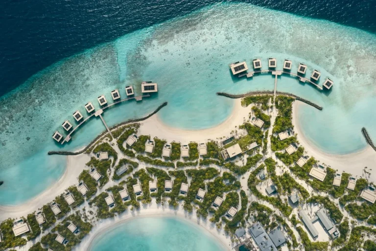 Aerial view of Patina Maldives on the Fari Islands, a curving island of beach villas with overwater villas off the north tip, North Malé Atoll