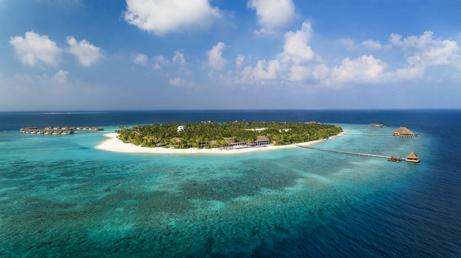 Aerial view of Velaa Private Island in Noonu Atoll, a round green island ringed by white sand, a turquoise lagoon and overwater villas on the reef edge