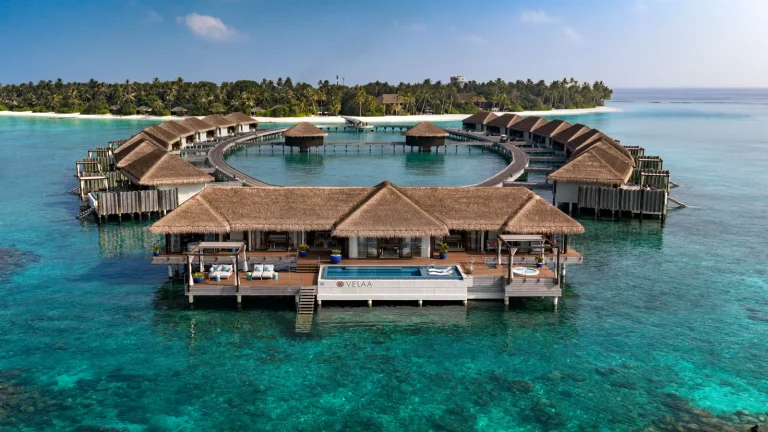 Aerial view of the overwater villa cluster at Velaa Private Island, thatched water pool villas around a turquoise lagoon in Noonu Atoll, Maldives