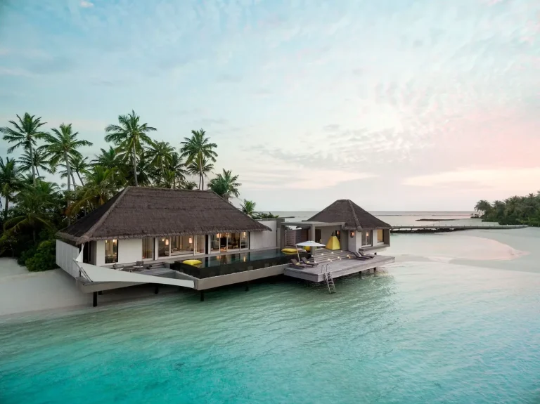 Thatched two-bedroom Lagoon Garden Villa with a long deck standing over a pale lagoon at sunset, Cheval Blanc Randheli, Noonu Atoll, Maldives