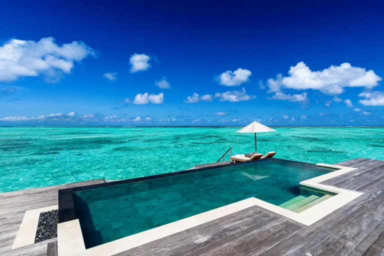 Timber overwater deck with an infinity pool, parasol and sun loungers above a turquoise lagoon at Gili Lankanfushi, North MalΓ© Atoll, Maldives