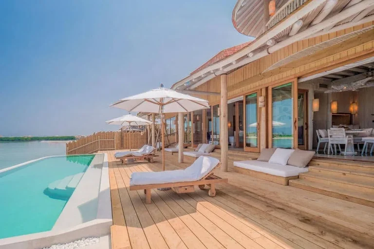 Wide timber deck with sun loungers, parasols and a long private pool over the Medhufaru lagoon at a Soneva Jani Water Retreat, Noonu Atoll, Maldives