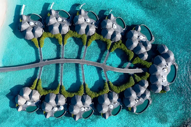 Top-down drone view of thatched overwater Ocean Houses with private pools linked by a timber jetty at The Nautilus Maldives, Baa Atoll
