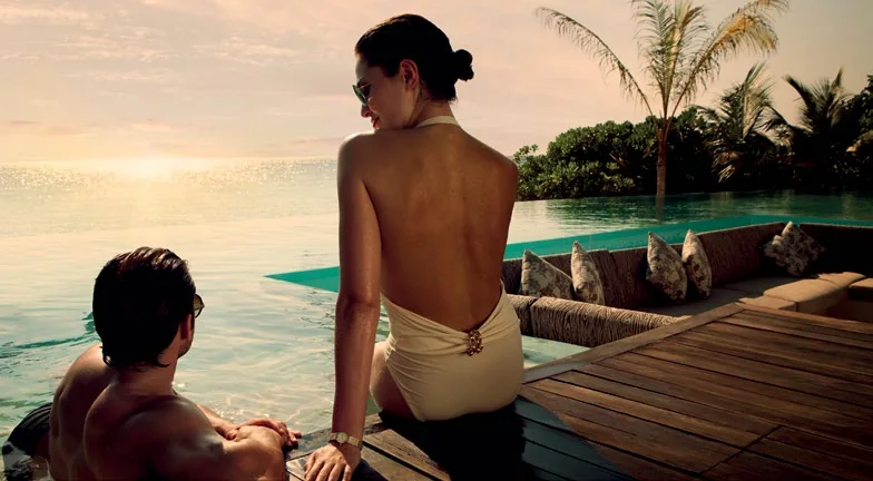 Couple sitting on the edge of the pool deck at sunset among palms, Coco Privé Kuda Hithi, Maldives