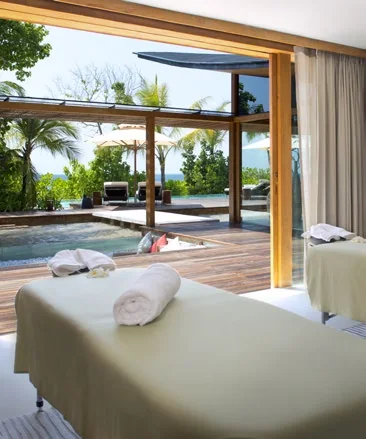 Massage table with folded towels in an open room facing a pool and garden, Coco Privé Kuda Hithi, Maldives