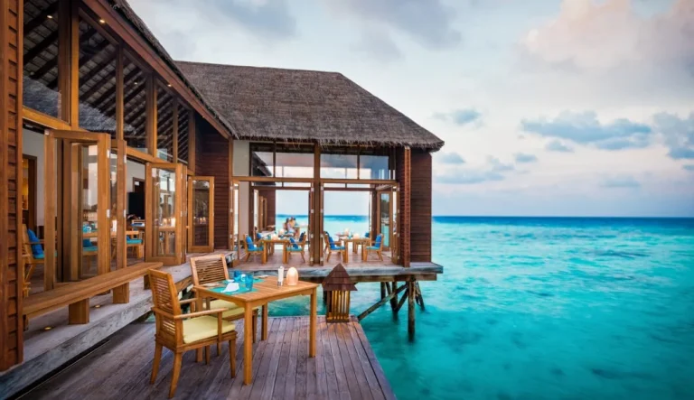 Overwater restaurant deck with tables and a thatched roof above turquoise water, Mandhoo, Conrad Maldives Rangali Island