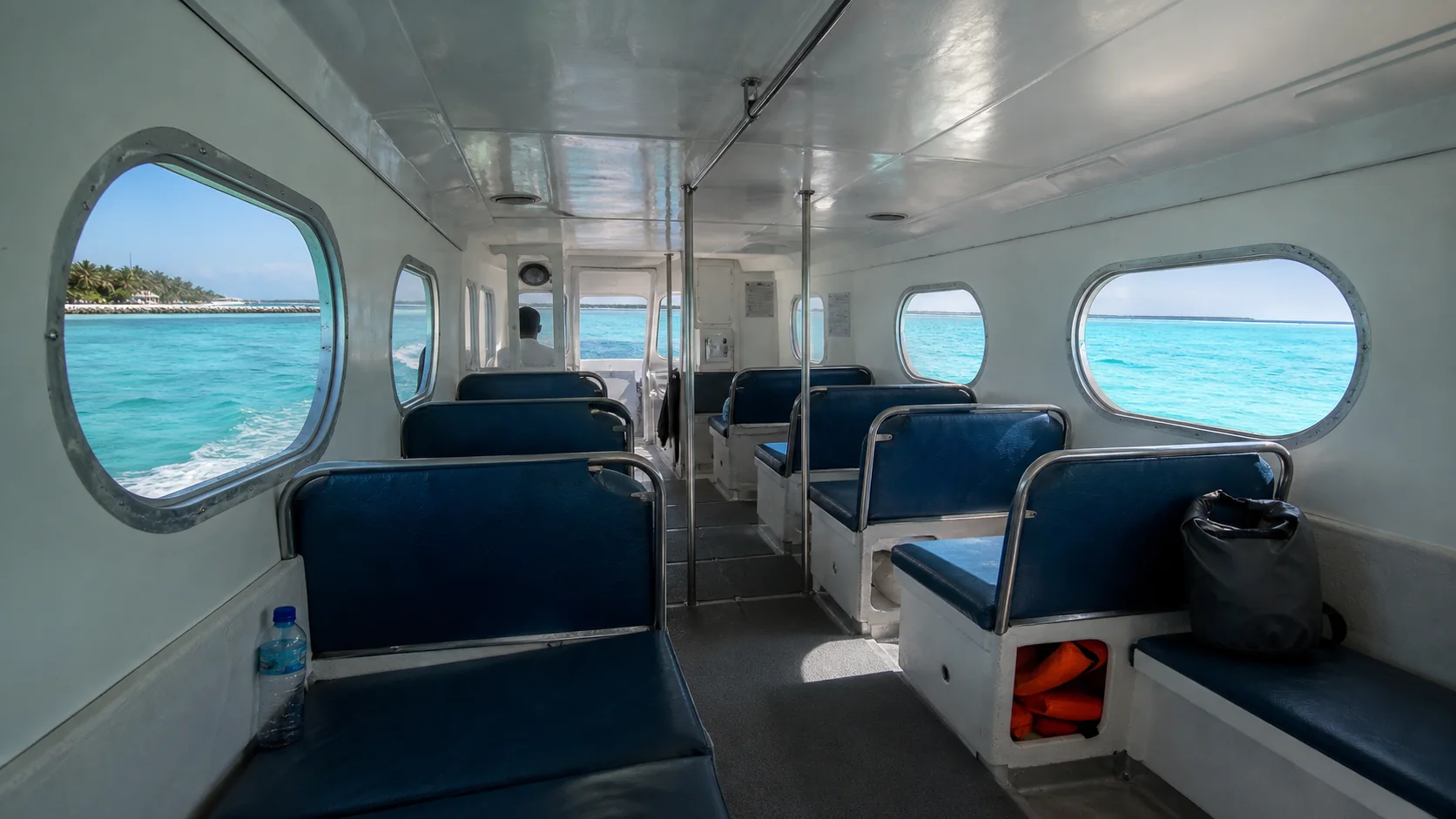 Interior of a Maldivian speedboat cabin showing passenger seating, with ocean views through windows