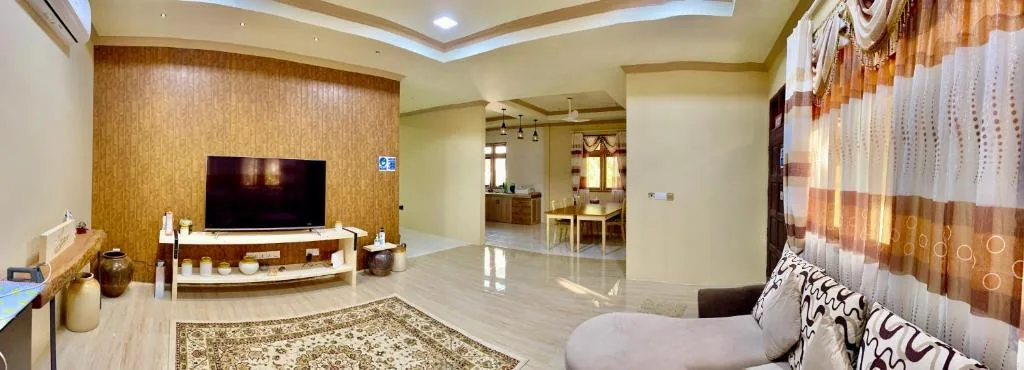 Open-plan living area with wood-paneled accent wall, flat-screen TV, patterned sofa and adjoining dining area at Endhaa, Divers Home at Endhaa Divers Home, Fuvahmulah, Maldives