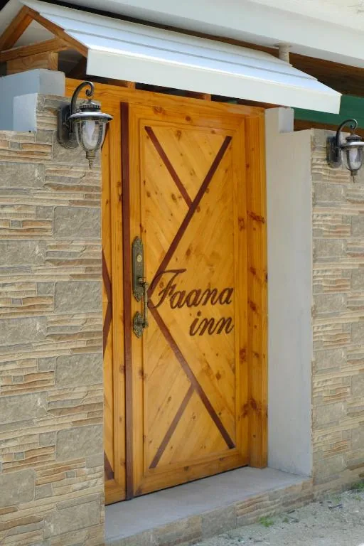 Wooden door with X-cut inlay, brass handle and 'Faana inn' lettering set in stone wall with wall lanterns and awning at Faana Inn, Fulhadhoo, Maldives