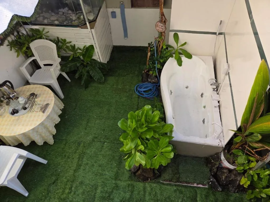 Outdoor patio with artificial turf, bistro table with chairs, plastic chairs, potted plants and an outdoor bathtub at Fehivilla Residence Inn, Dhangethi, Maldives