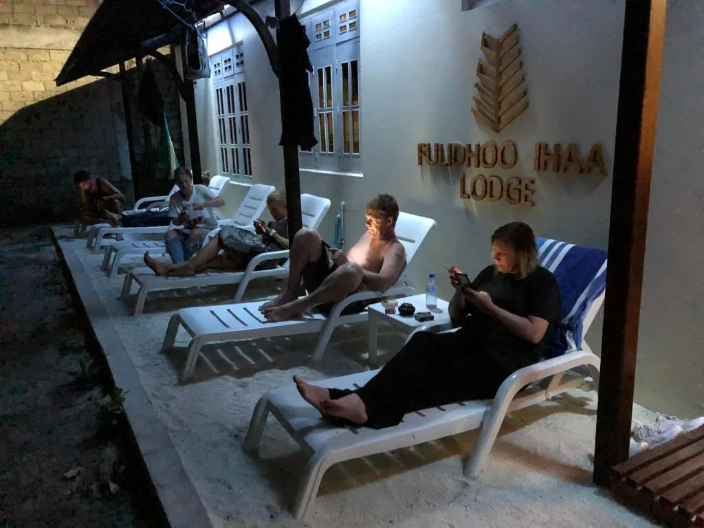 Guests on lounge chairs at FULDHAA LODGE with sandy courtyard, shaded dining table and hanging clothesline at Fulidhoo Ihaa Lodge, Fulidhoo, Maldives
