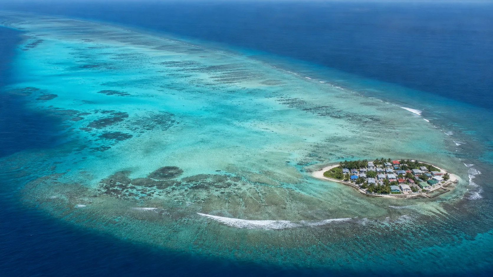 Aerial view of Gaafaru island in Kaafu Atoll, Maldives, showing the small inhabited island on the eastern edge of the large elliptical reef and turquoise lagoon