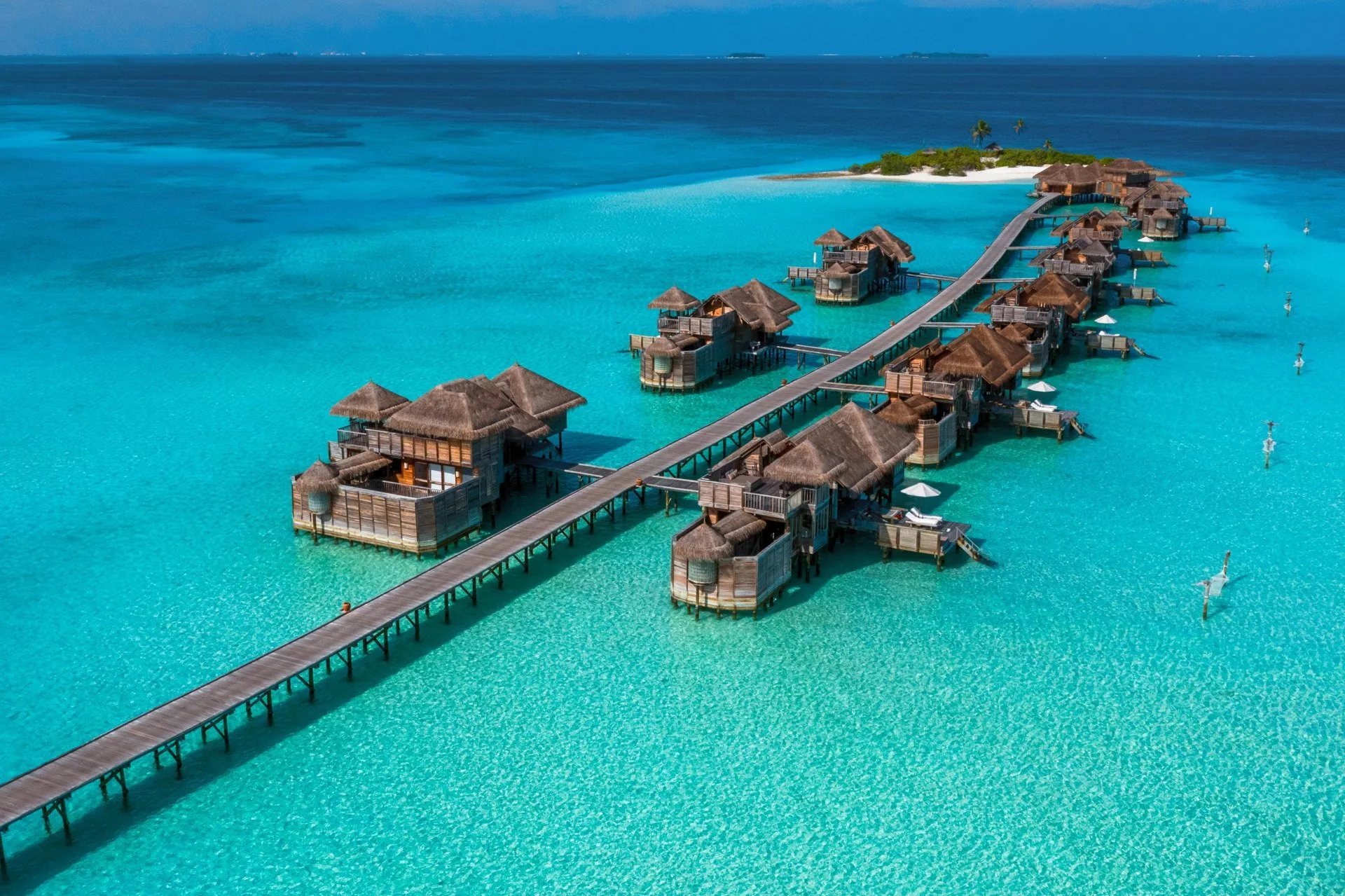 Aerial view of thatched overwater villas along a timber jetty in a turquoise lagoon at Gili Lankanfushi, North Malé Atoll