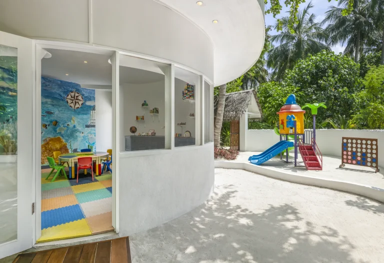 Bright white kids club building with a colourful slide and play area under palms at The Halcyon Private Isles Maldives