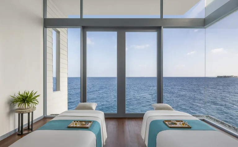 Overwater spa treatment room with two massage beds and floor-to-ceiling windows onto the ocean at The Halcyon