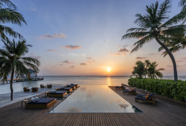 Long infinity pool with loungers facing the sun setting over the ocean at The Halcyon Private Isles Maldives
