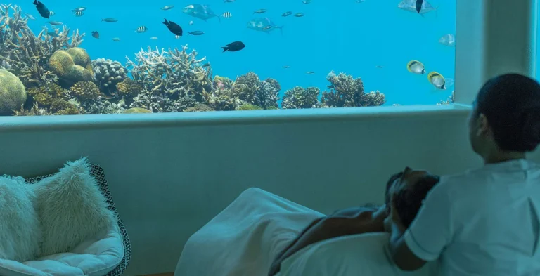 Guest lying on a treatment bed beside a large underwater window onto the reef, Huvafen Fushi, Maldives