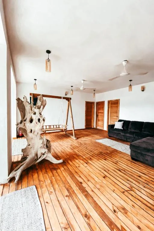 Open-plan living room with live-edge wooden swing, hardwood floors, L-shaped sofa, ceiling fans and wall sconces at Island Zephyr, Goidhoo, Maldives