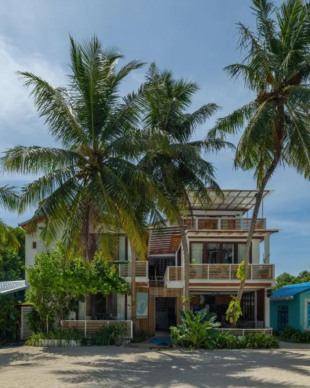 Three-story beachfront guesthouse with balcony, shaded upper terrace, palm trees and sandy shore at Kinan Retreat, Fulidhoo, Maldives
