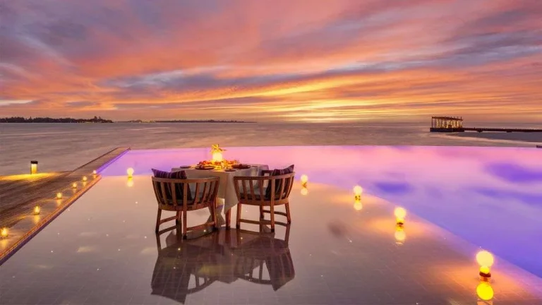 Candlelit table for two on the edge of an infinity pool at sunset at The Retreat at Kudadoo Maldives Private Island
