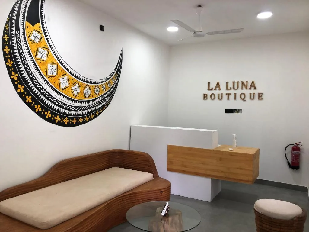 LUNA BOUTIQUE reception with wooden desk, round table, patterned wall mural, woven lounge chair and wall-mounted fan at La Luna Boutique Dhangethi, Dhangethi, Maldives