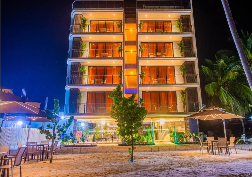 Beachfront hotel with illuminated balconies, ground-floor dining and outdoor umbrellas on sandy shore, palm trees at night at Lonuhiri, Dhigurah, Maldives