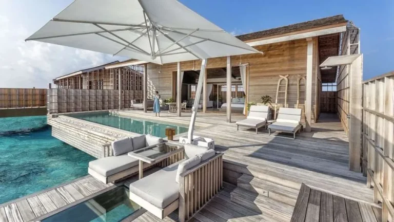Wooden deck of an overwater residence at Kudadoo Maldives Private Island with a private pool, sun loungers and a white parasol, Lhaviyani Atoll