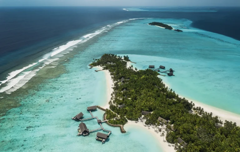 Aerial view of the long island of One&Only Reethi Rah with white beaches, palm forest and overwater villas on a jetty, North Malé Atoll