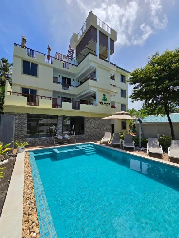 Four-story yellow hotel with rooftop pool, balcony rooms, shaded pool loungers and palm trees at Madi Grand Guest House, Fulidhoo, Maldives