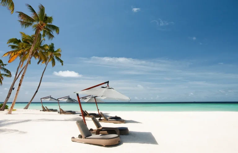 White sand beach with a hammock chair and parasol under leaning palms at Constance Halaveli, North Ari Atoll, Maldives