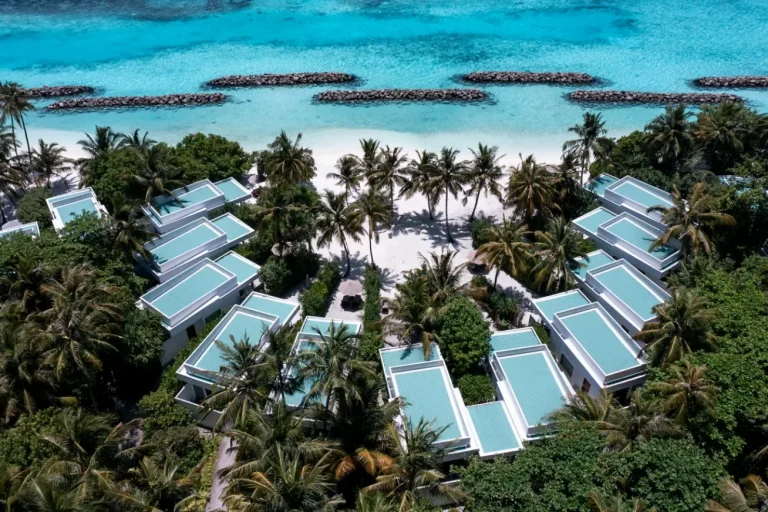 Aerial view of beach villas set among palms along a white beach and turquoise lagoon at Niva Dhigali Maldives, Raa Atoll