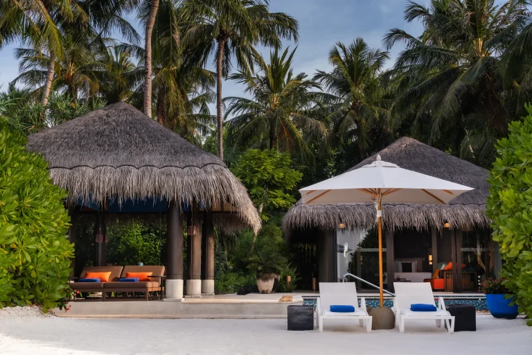 Thatched beach pool villa with sun loungers and a parasol on white sand among palms at Velaa Private Island, Noonu Atoll, Maldives
