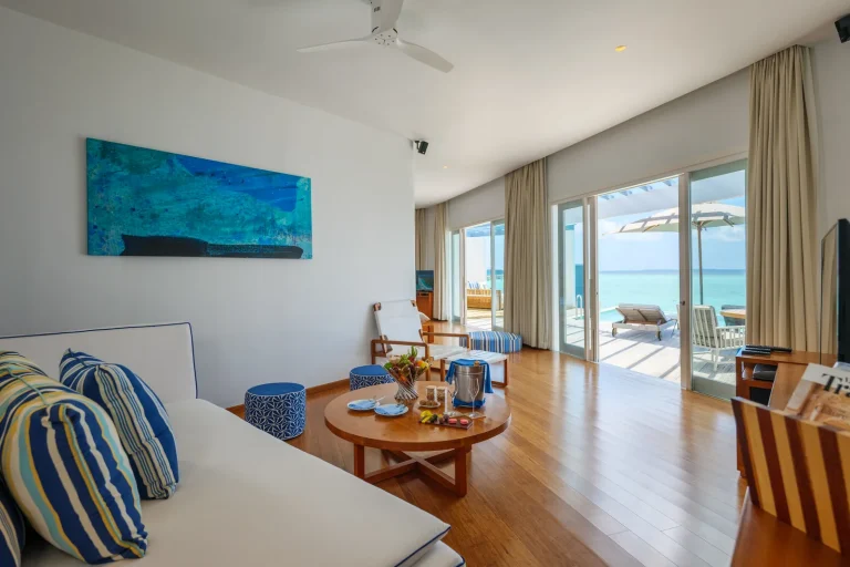 Bright living room of an Amilla Lagoon Water Pool Villa with sliding doors open to the deck and lagoon, Baa Atoll, Maldives