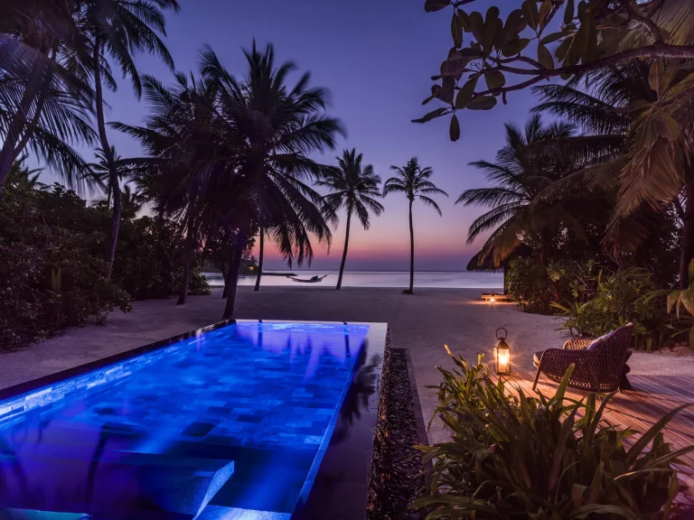 Lit private pool and deck of a Beach Villa with Pool under palms at dusk at One&Only Reethi Rah, North MalΓ© Atoll, Maldives