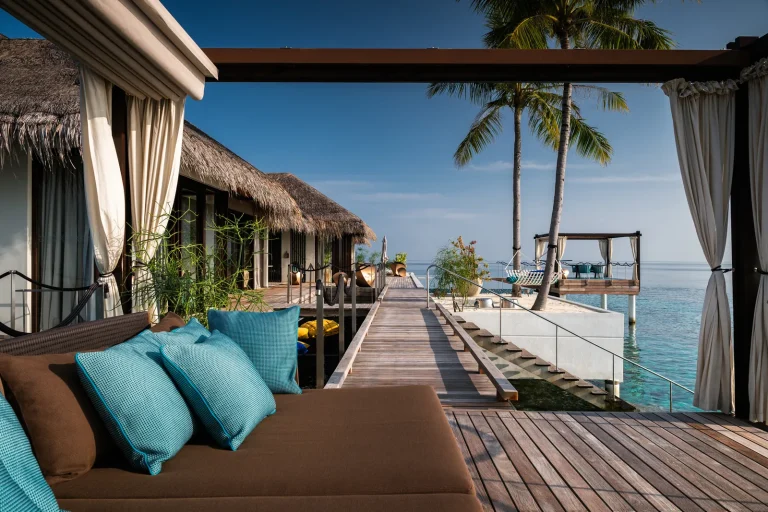 Shaded terrace with cushions on the jetty leading to the Romantic Pool Residence over the lagoon at Velaa Private Island, Noonu Atoll
