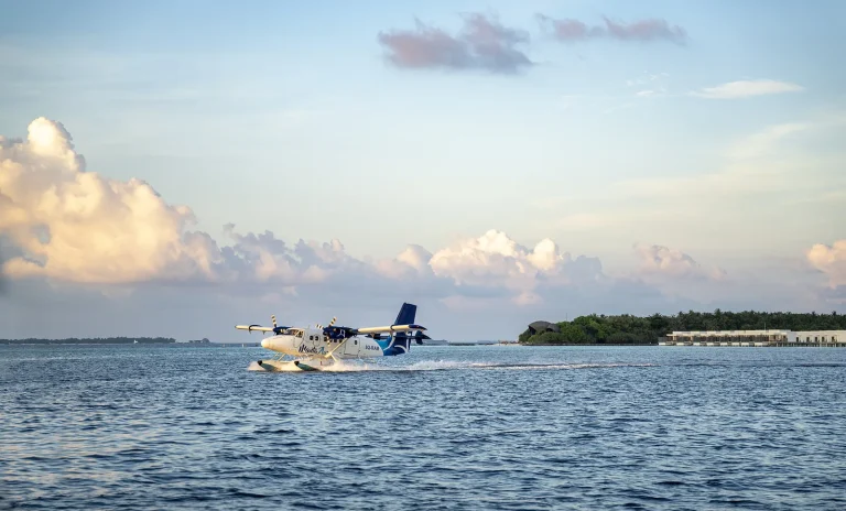 Twin Otter seaplane taking off from a calm lagoon beside a resort island, Raa Atoll, Maldives