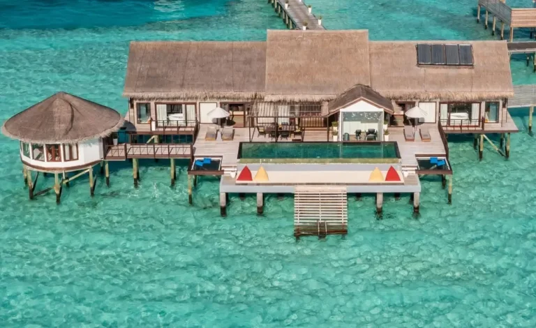 Large overwater residence with a long private pool, two pavilions and a wide timber deck above a clear lagoon at OZEN LIFE MAADHOO, Maldives