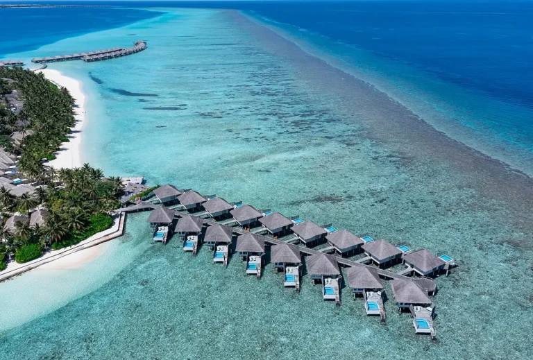 Aerial view of the long water villa jetty at Velassaru running from the beach across a shallow lagoon towards the reef, South MalΓ© Atoll, Maldives