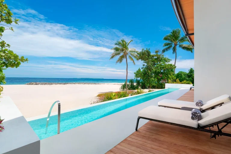 Long private infinity pool and loungers on the deck of a beach residence facing palms and white sand at The Westin Maldives Miriandhoo Resort, Baa Atoll